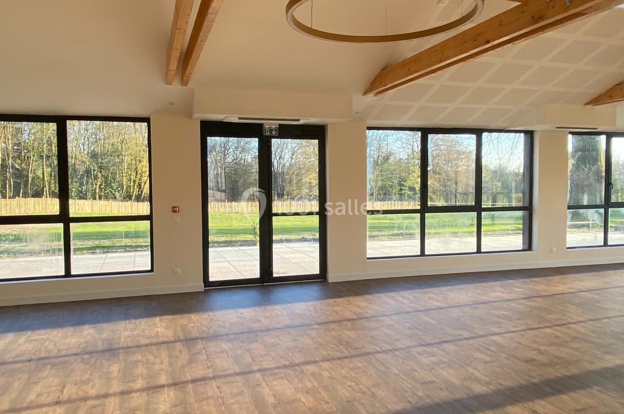Salle lumineuse avec parquet en bois, grandes baies vitrées donnant sur un espace extérieur arboré.