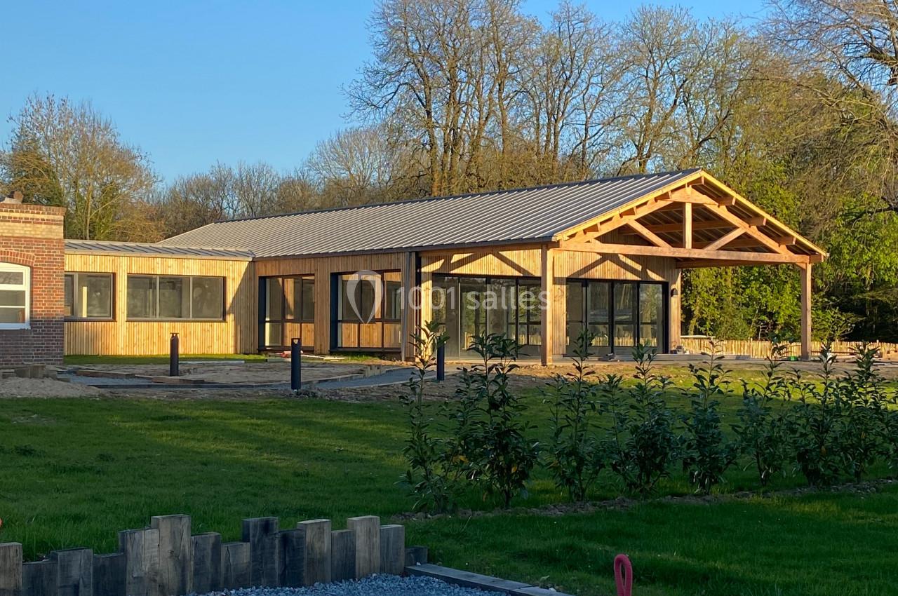 Bâtiment moderne en bois avec de grandes baies vitrées, entouré de pelouse et d'arbres sous un ciel dégagé.