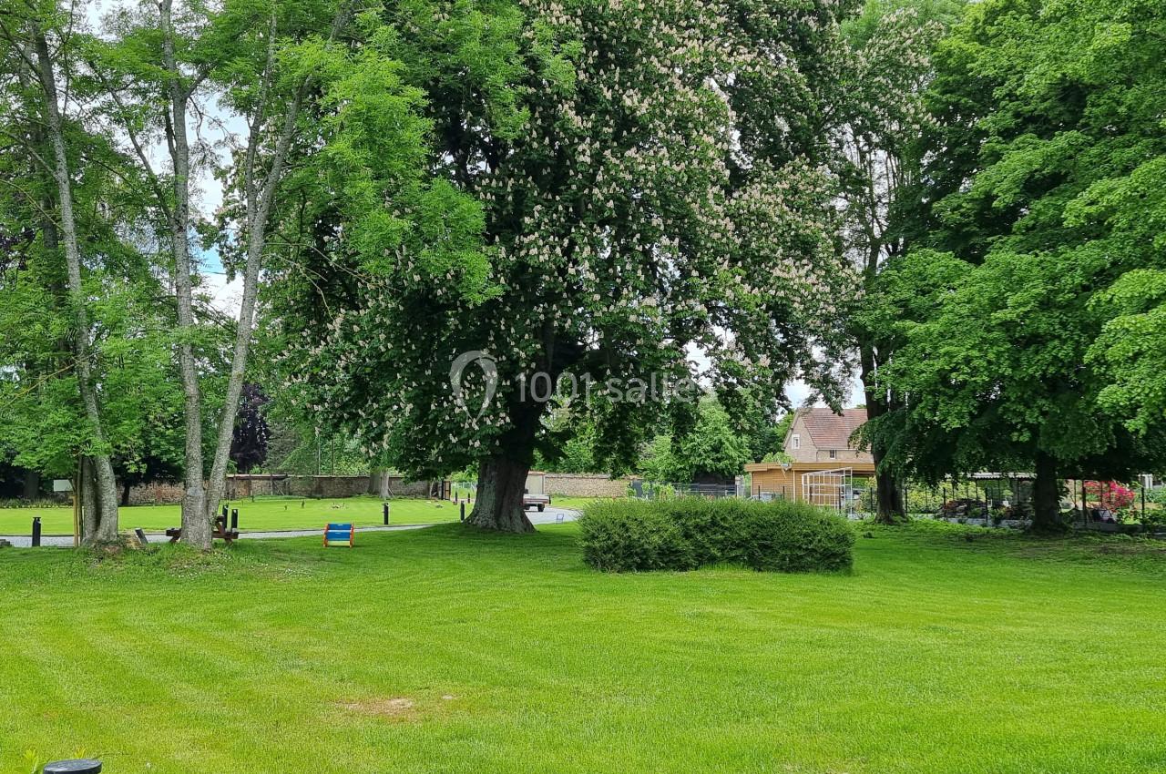 Pelouse verdoyante entourée d'arbres feuillus, avec une maison en arrière-plan partiellement visible.