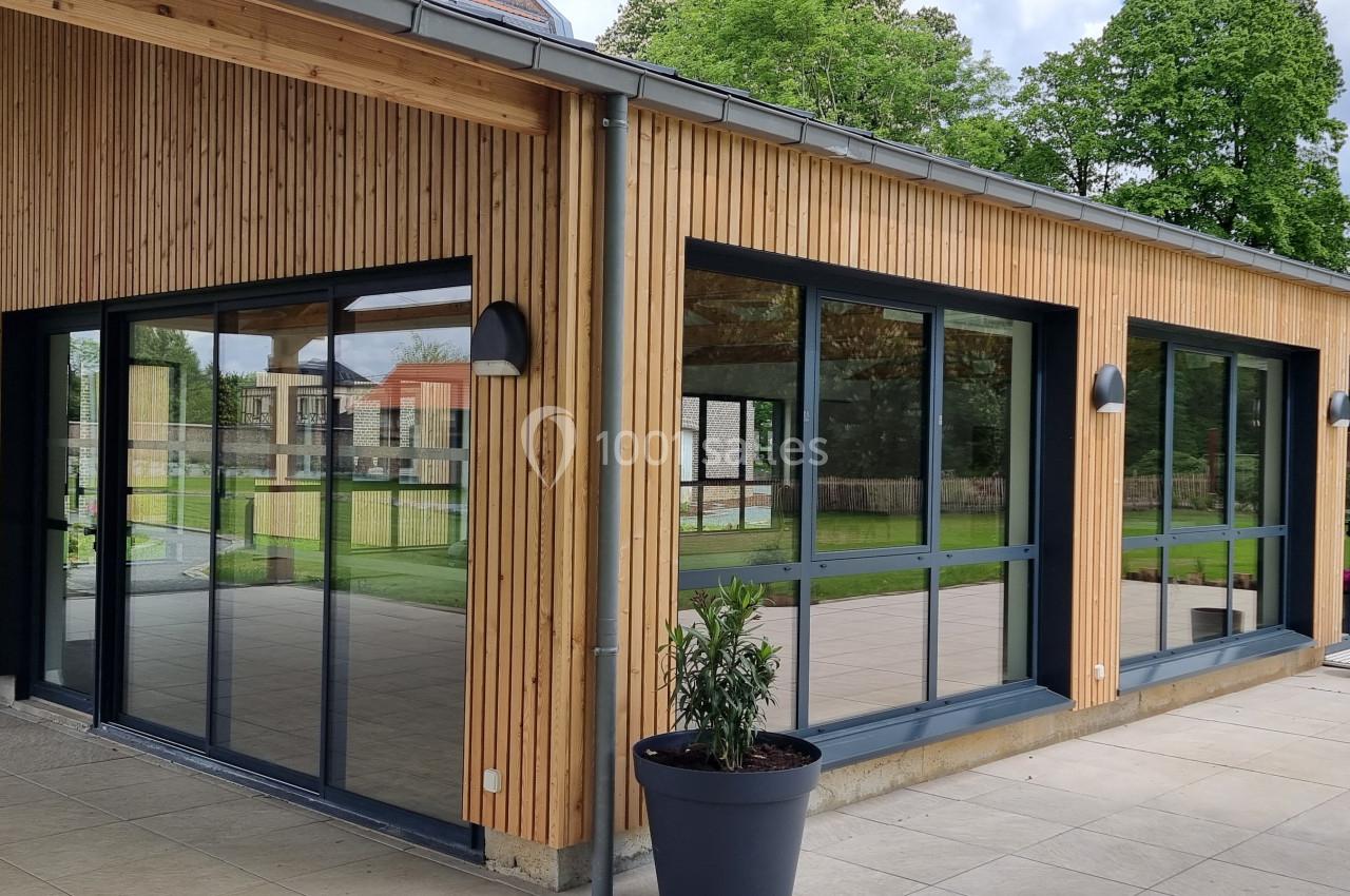 Bâtiment moderne en bois avec de grandes baies vitrées donnant sur une terrasse et un espace vert.