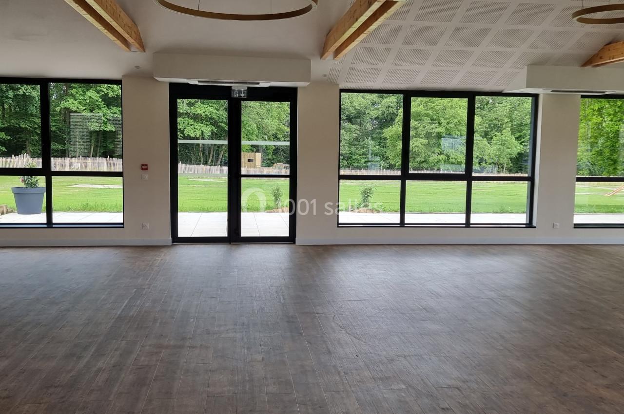 Salle lumineuse avec parquet, grandes baies vitrées donnant sur un jardin verdoyant.