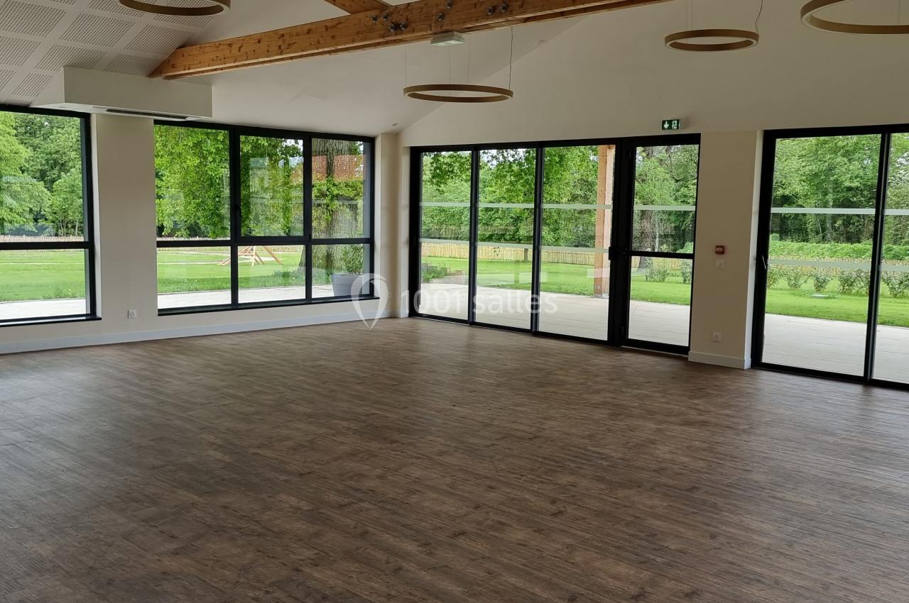 Salle lumineuse avec parquet en bois, grandes baies vitrées donnant sur un jardin verdoyant.