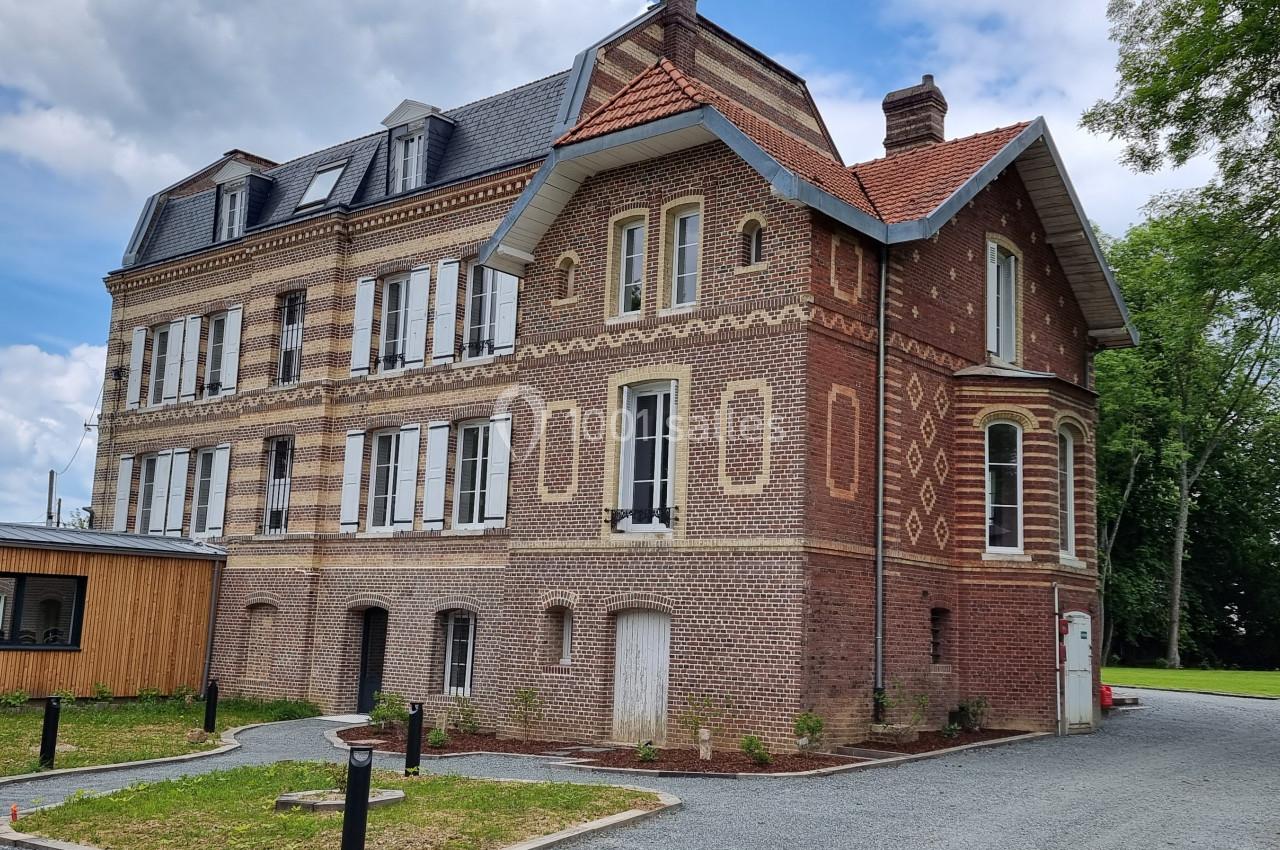 Bâtiment en briques rouges à plusieurs étages, entouré de verdure, avec une allée en gravier au premier plan.