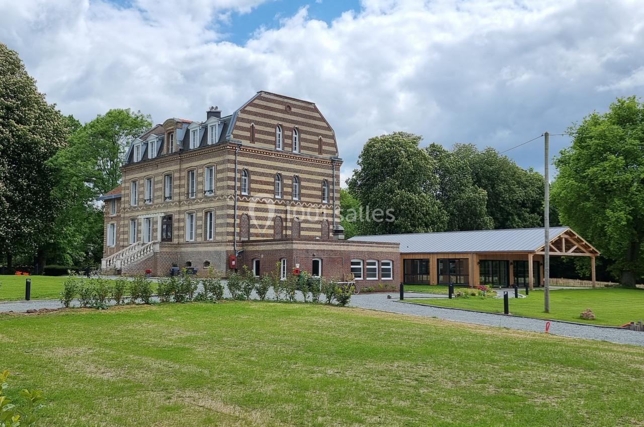 Bâtiment en briques entouré de pelouses et d'arbres, avec une annexe moderne en bois à droite.