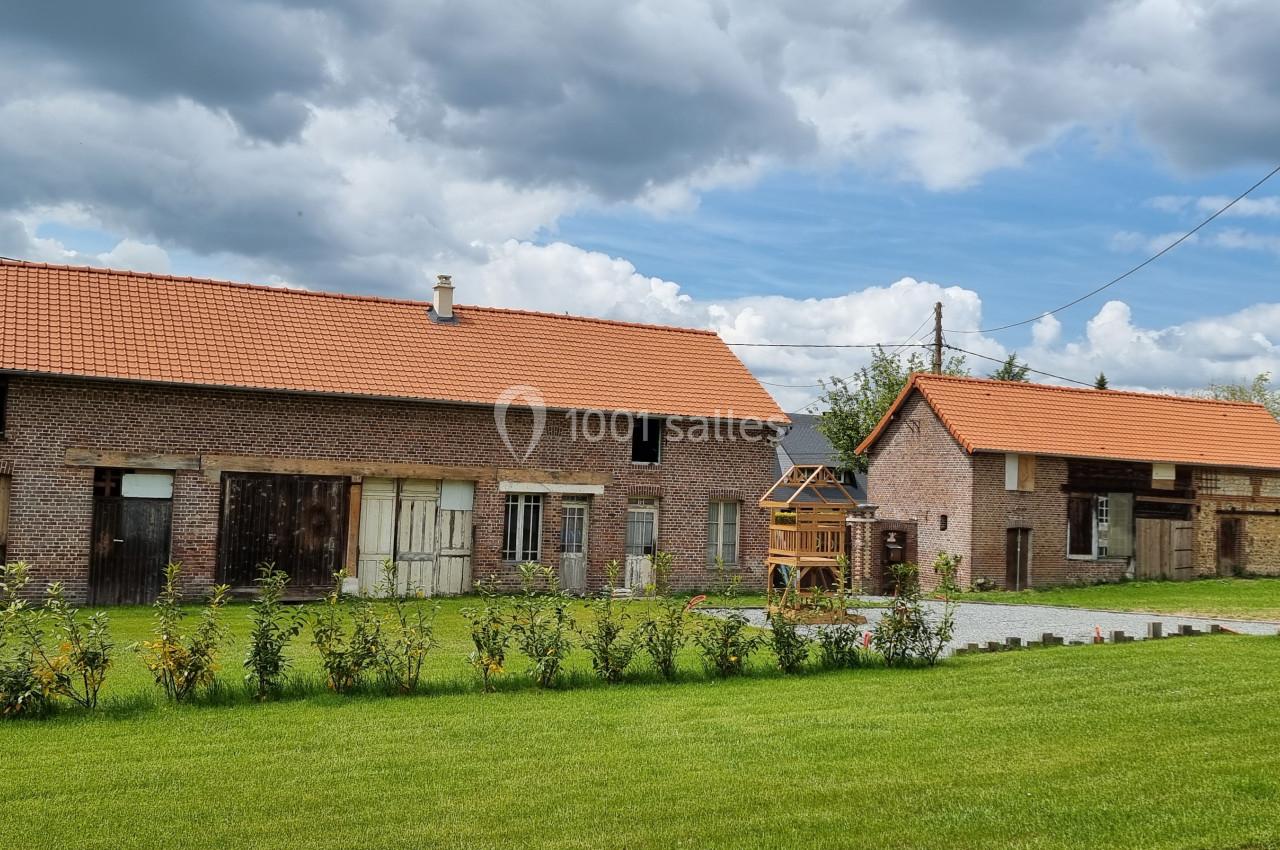 Bâtiments en briques avec toits en tuiles rouges, entourés de pelouses et d'arbustes sous un ciel partiellement nuageux.