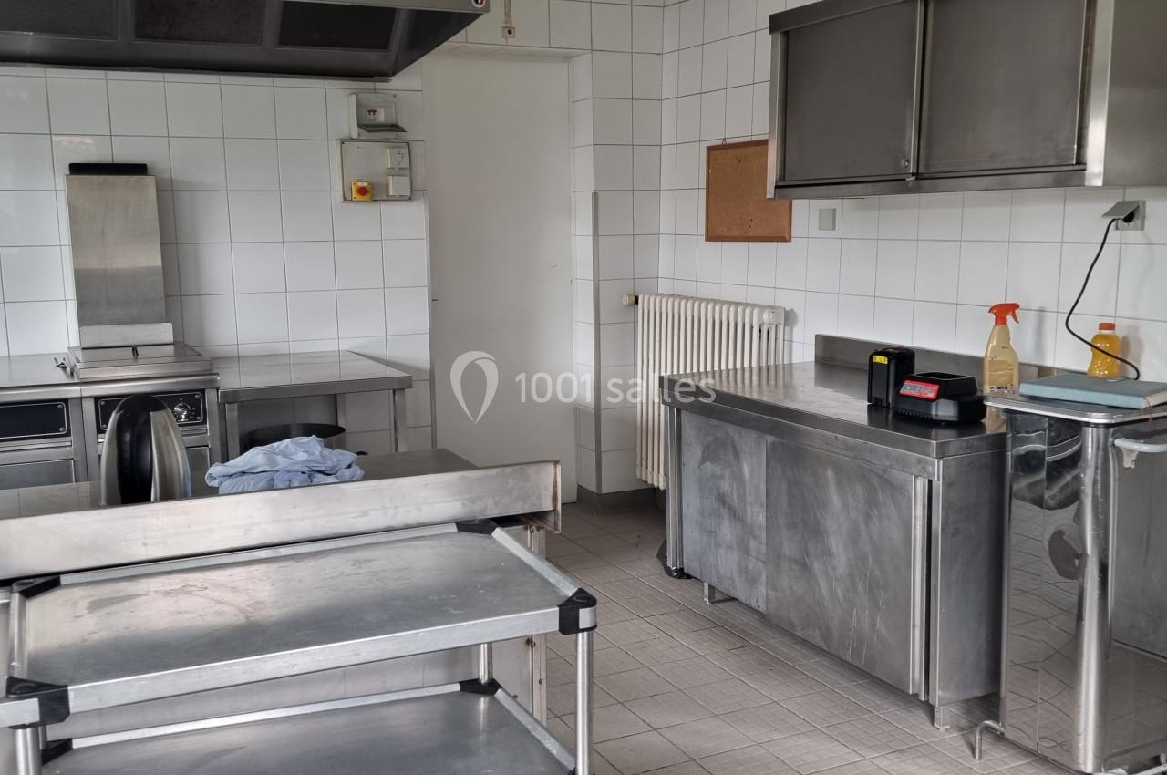 Cuisine professionnelle avec équipements en inox, murs carrelés blancs, extincteur et produits de nettoyage visibles.