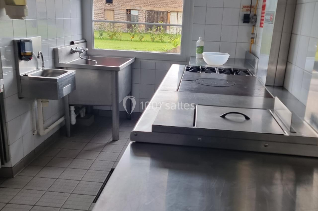 Cuisine professionnelle avec plan de travail en inox, évier, plaques de cuisson et fenêtre donnant sur un extérieur.