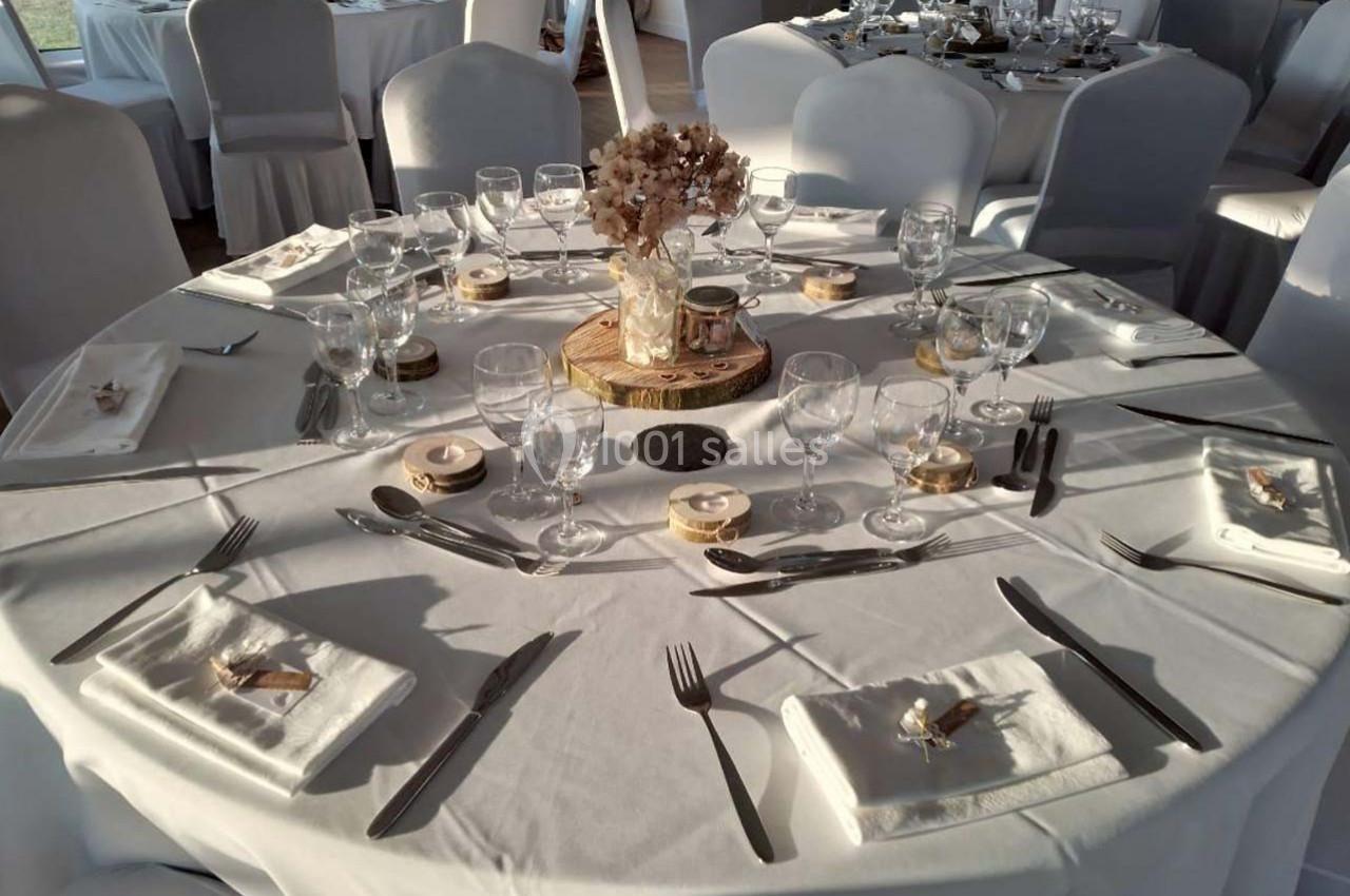 Table ronde dressée pour un événement, avec nappes blanches, couverts, verres et décoration florale centrale.