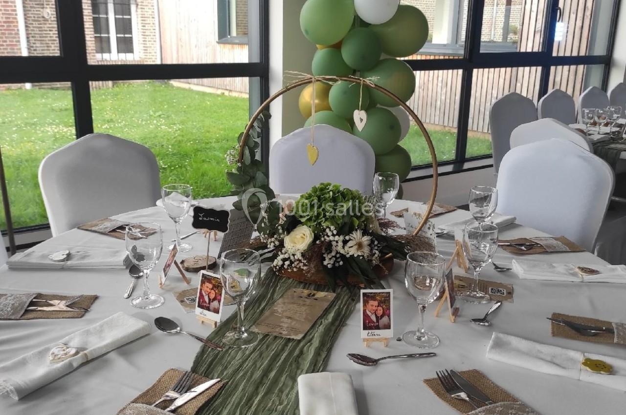 Table de réception décorée avec nappes blanches, chemin de table vert, compositions florales et ballons verts en arrière…