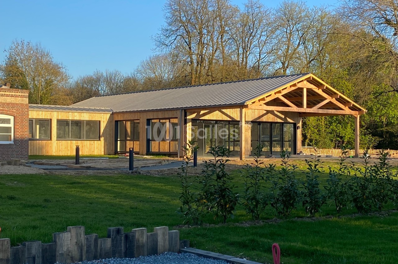 Bâtiment moderne en bois avec de grandes baies vitrées, entouré de verdure et éclairé par une lumière naturelle.