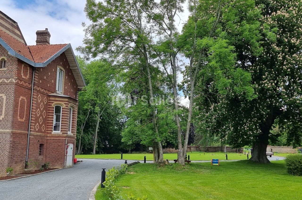 Maison en briques rouges avec un toit en ardoise, entourée d'arbres et d'une pelouse bien entretenue.