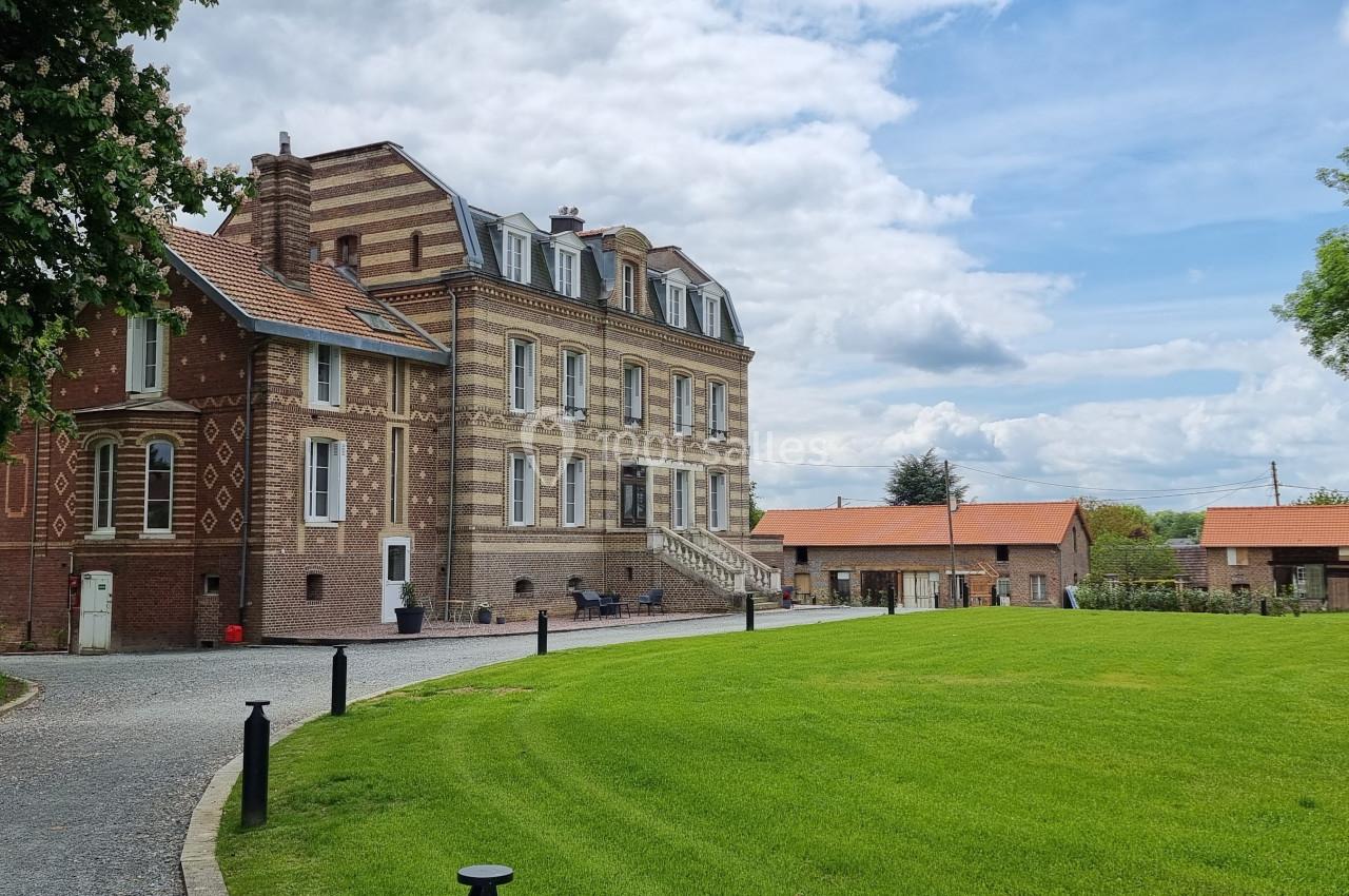 Bâtiment en briques rouges et beiges entouré d'une pelouse verte, sous un ciel partiellement nuageux.