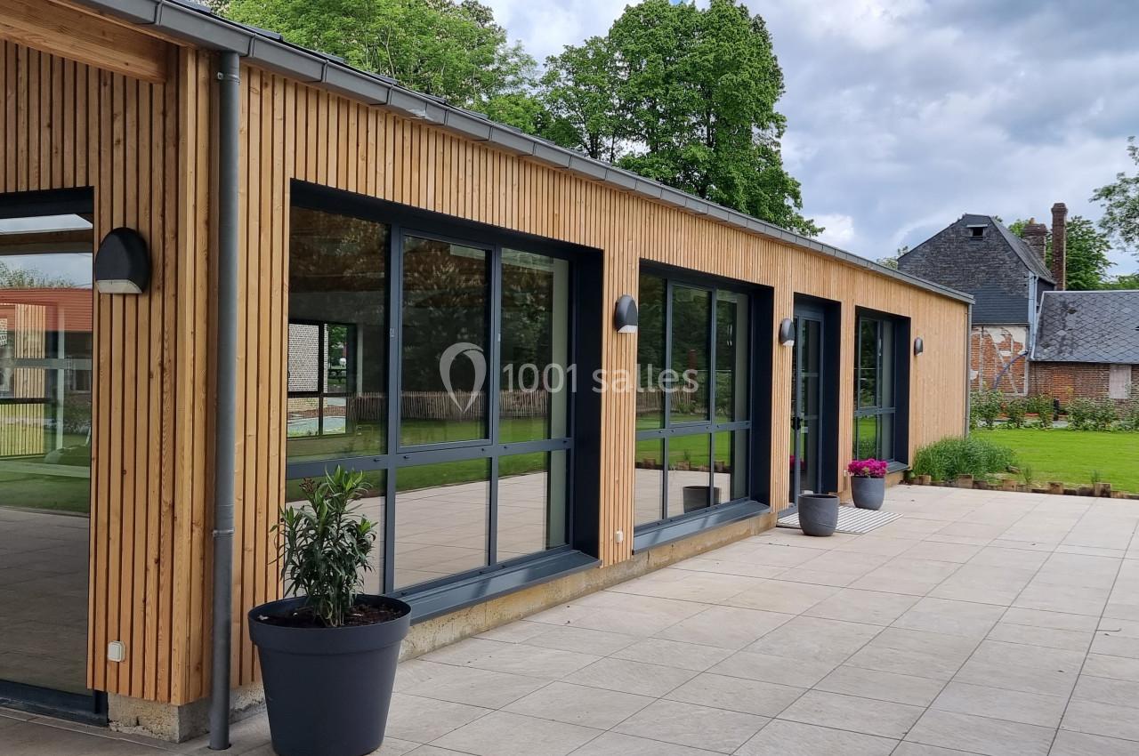 Bâtiment moderne en bois avec de grandes baies vitrées, entouré d'une terrasse et d'un jardin verdoyant.