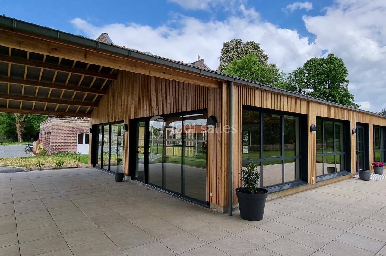 Bâtiment moderne en bois avec de grandes baies vitrées, entouré d'une terrasse et d'un jardin verdoyant.