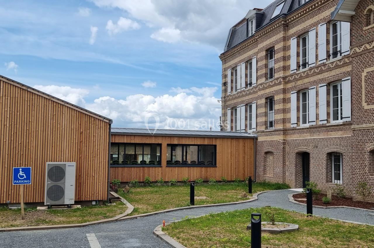 Bâtiment en briques et extension en bois avec chemin accessible et panneau indiquant un parking pour personnes handicapées.