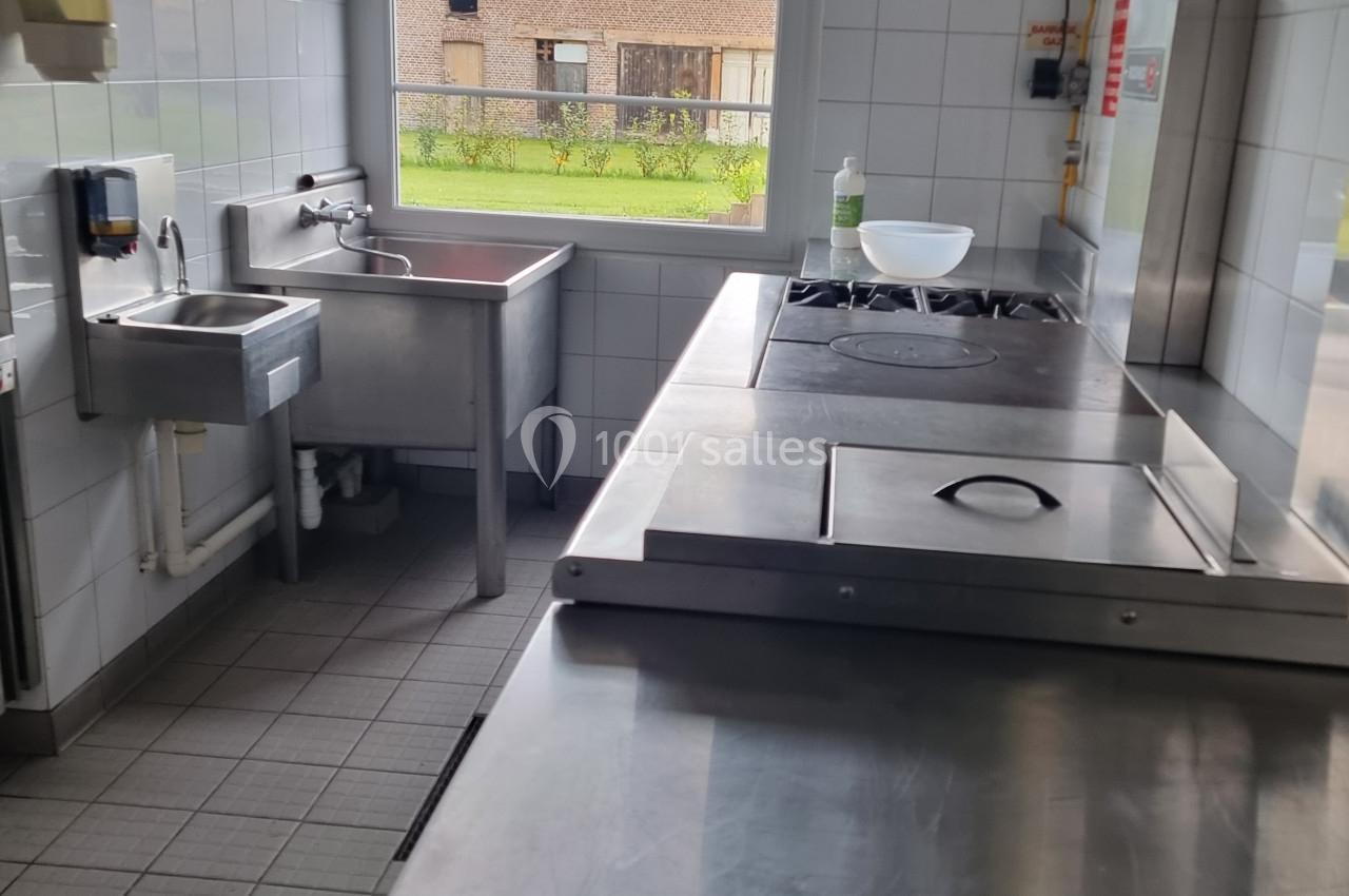 Cuisine professionnelle avec plan de travail en inox, évier, plaques de cuisson et fenêtre donnant sur un extérieur.