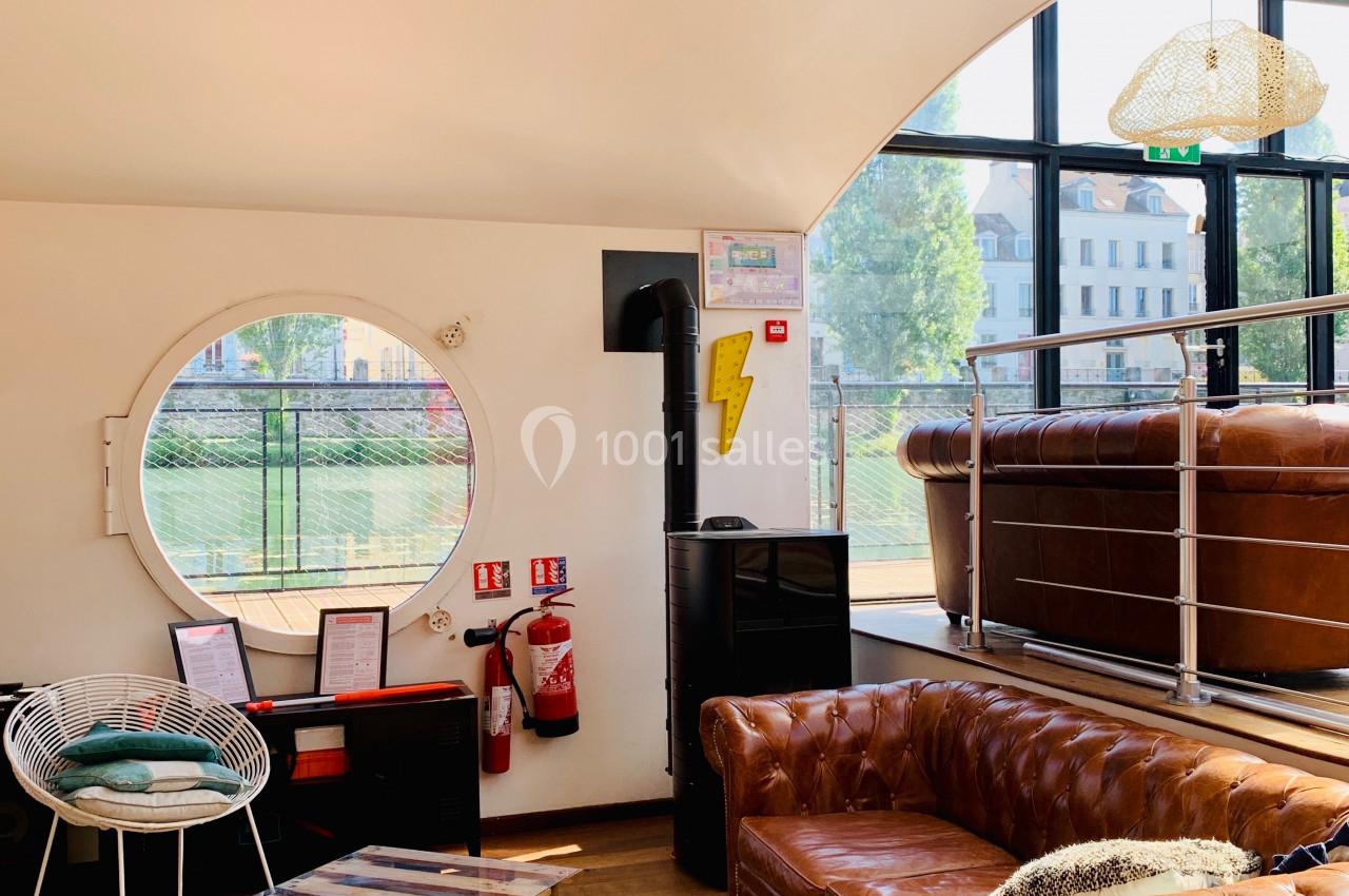 Salon lumineux avec canapé en cuir, table basse sur tapis en peau, grande fenêtre ronde et poêle à bois.