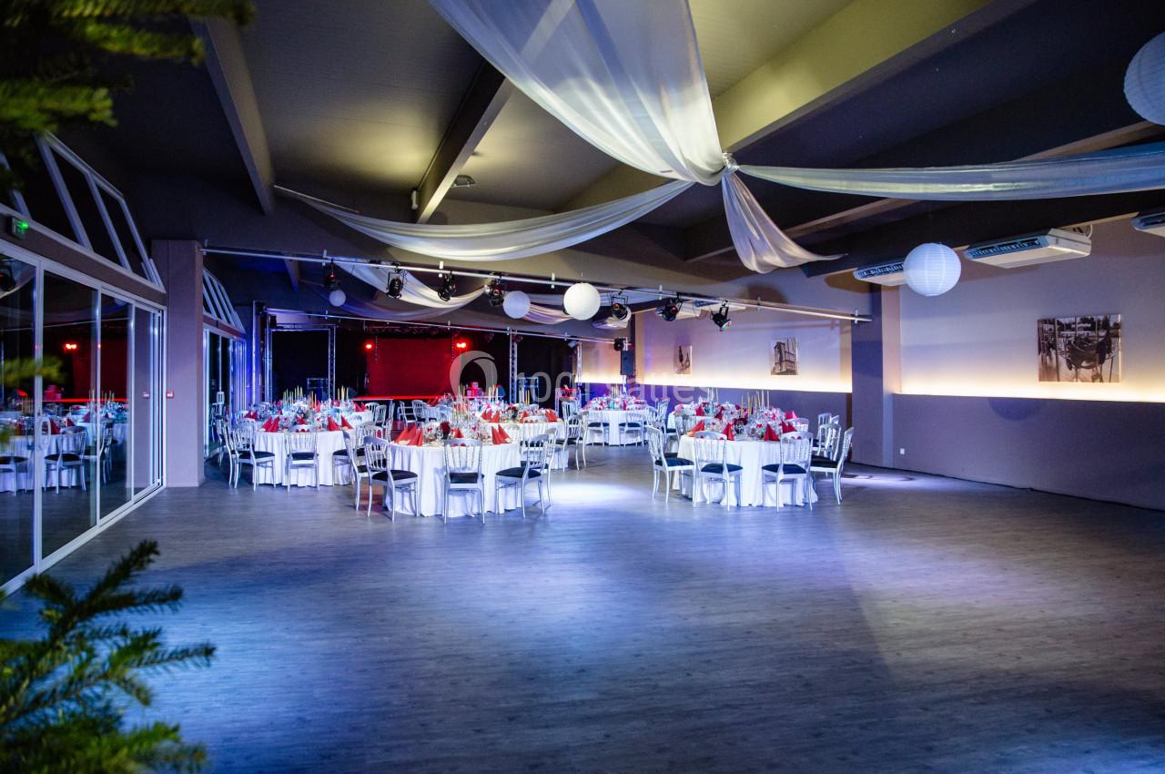 Salle de réception décorée avec des tables rondes dressées, des nappes blanches et des éclairages tamisés.