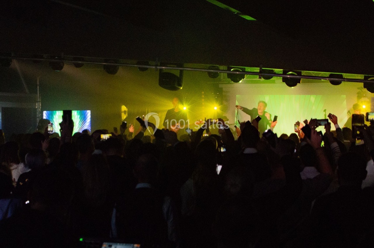 Foule assistant à un concert dans une salle sombre, éclairée par des jeux de lumière colorés sur scène.