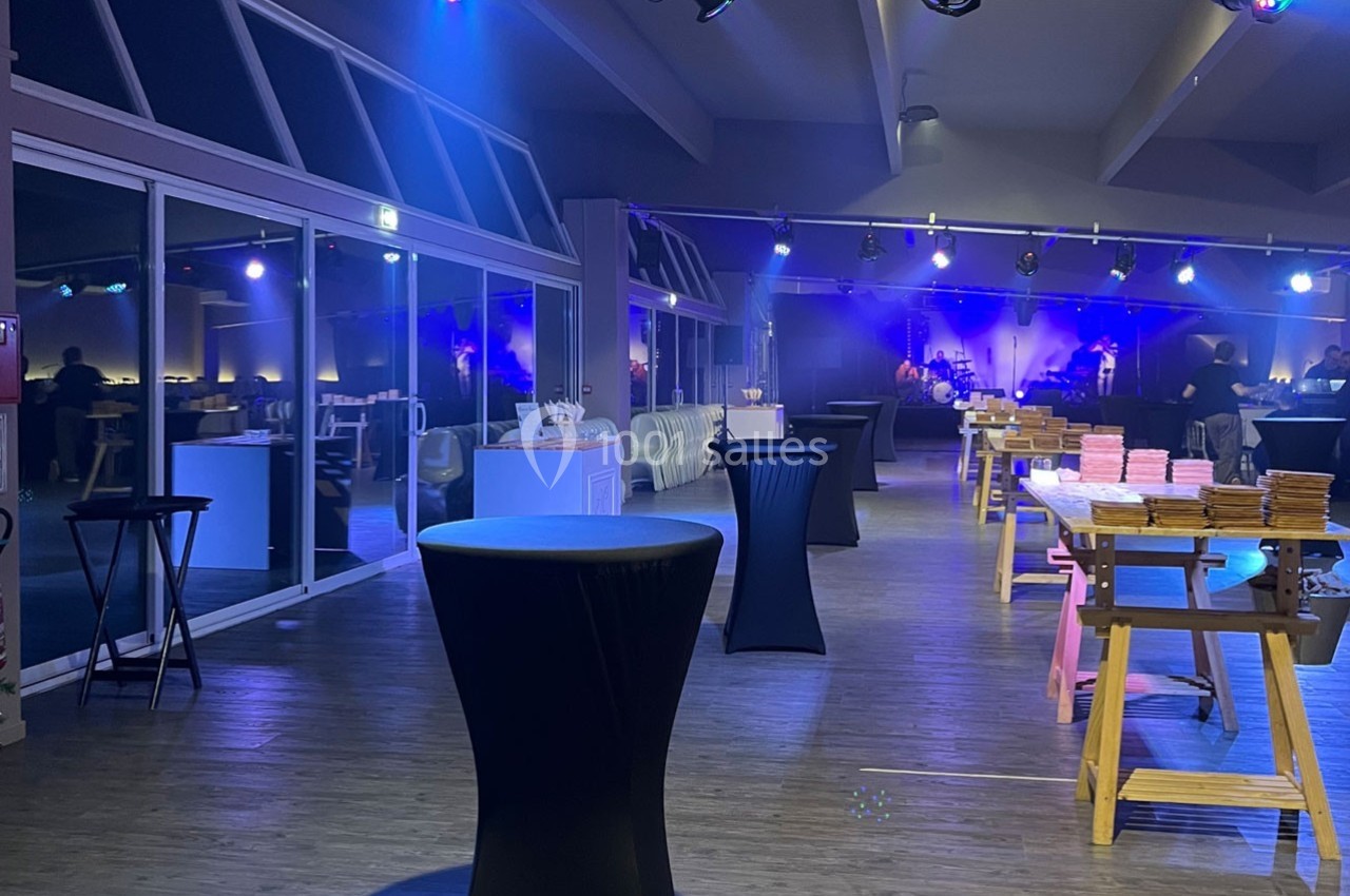 Salle de réception avec tables hautes, nappes noires et éclairage tamisé, préparée pour un événement.