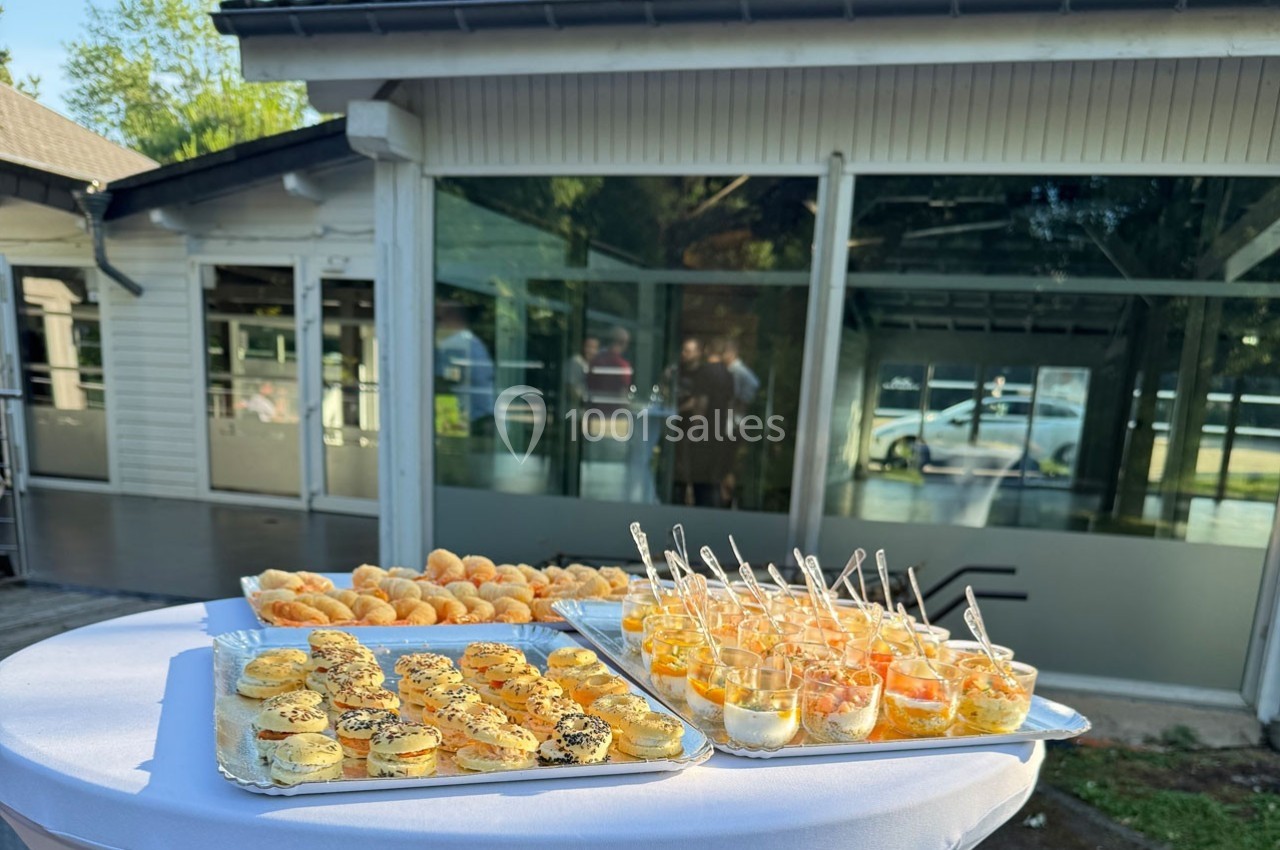 Plateaux de bouchées salées et verrines disposés sur une table en extérieur devant un bâtiment vitré.