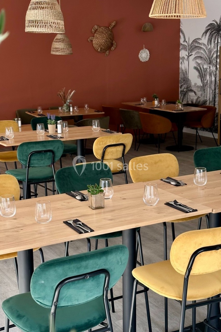 Salle de restaurant avec tables en bois, chaises colorées et décor mural tropical sur fond rouge et blanc.