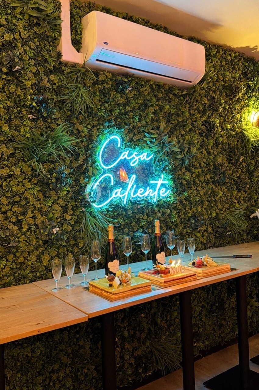 Mur végétal avec enseigne lumineuse ’Casa Caliente’, table en bois dressée avec flûtes à champagne et desserts.