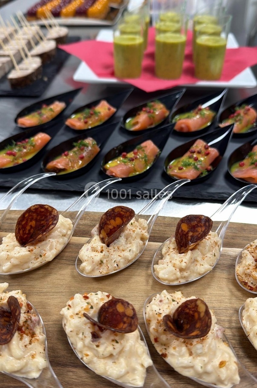 Cuillères apéritives garnies de risotto et chorizo, saumon mariné et verrines sur une table de buffet.