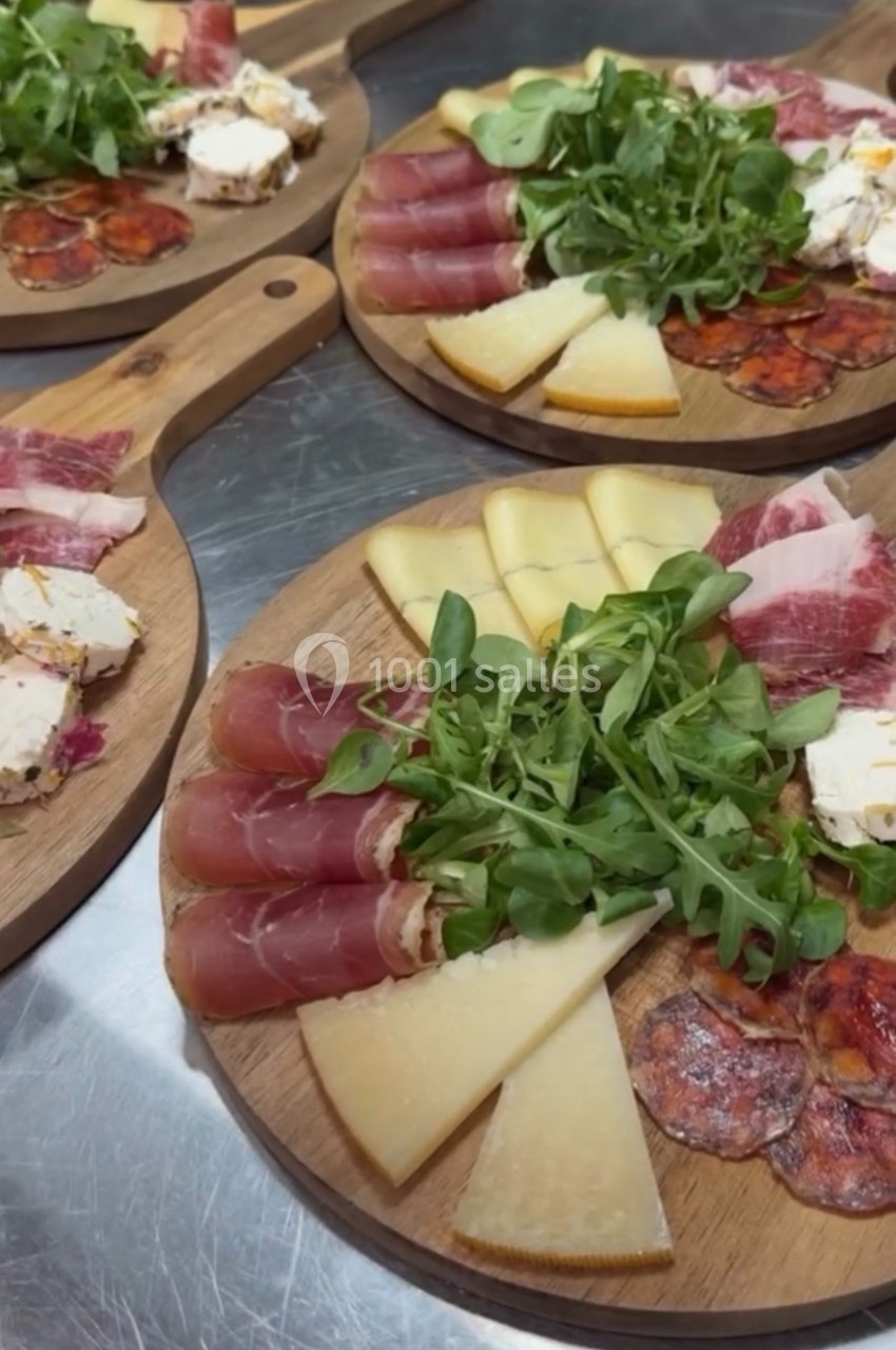 Plateaux en bois garnis de charcuteries, fromages variés, roquette et tranches de pain sur une table en inox.