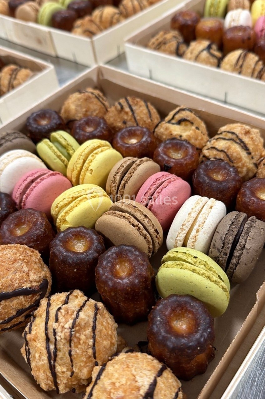 Assortiment de macarons colorés et de cannelés dorés présentés dans des boîtes en carton.
