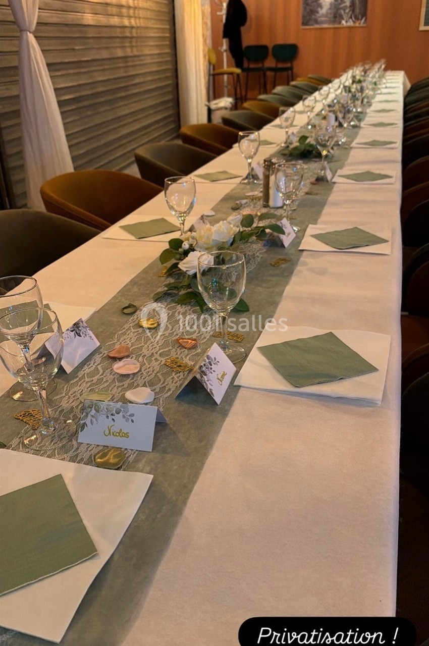 Table dressée pour un événement, avec nappes blanches, serviettes vertes, verres et décorations élégantes.