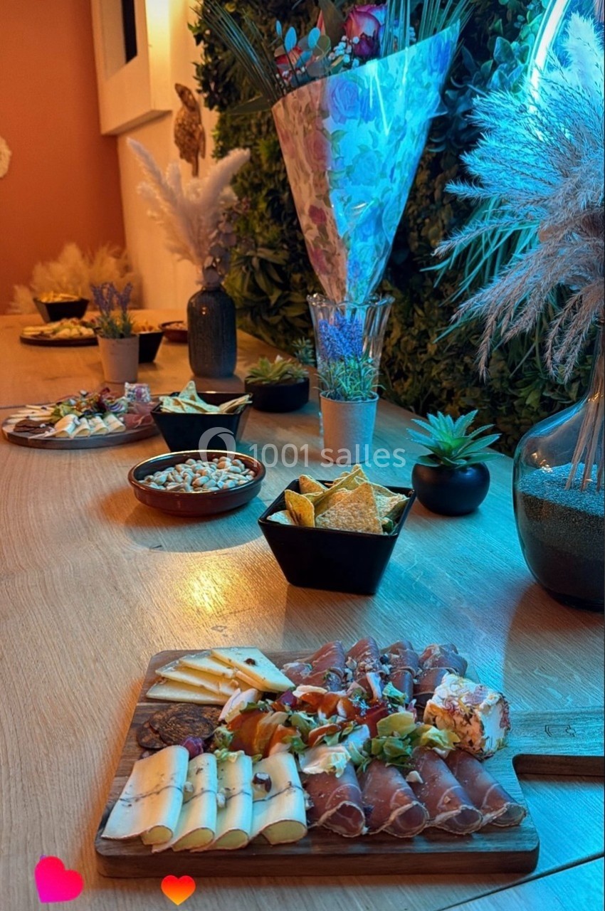 Plateau de charcuterie et fromages accompagné de bols d'apéritifs sur une table décorée de plantes et fleurs séchées.