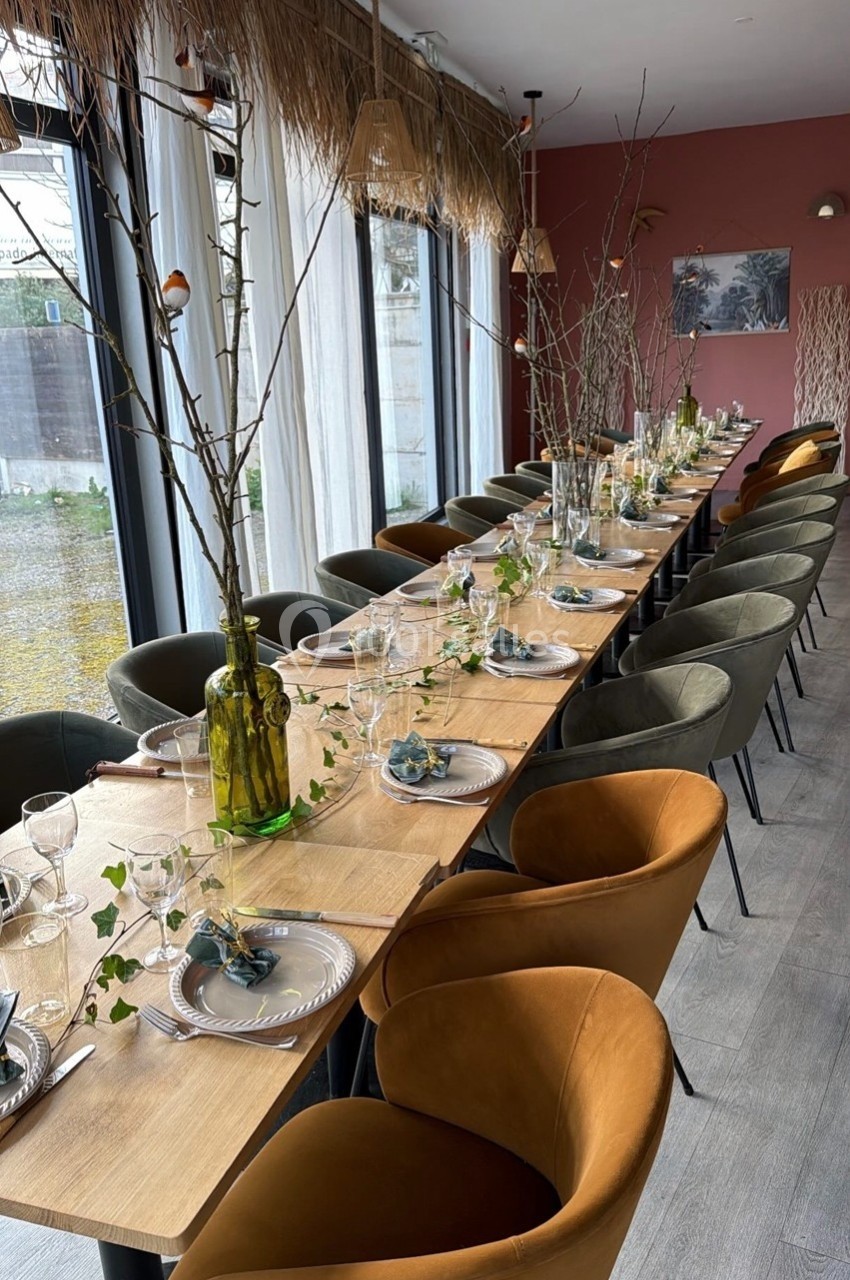 Table en bois décorée pour un repas, avec vaisselle élégante, branches et feuillage, entourée de chaises modernes.
