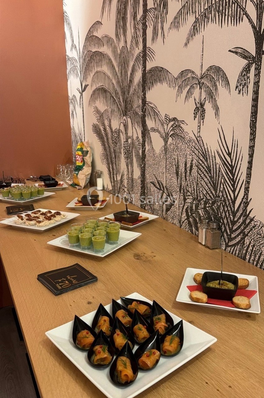 Buffet avec des amuse-bouches variés disposés sur une table en bois, décorée d'un mur à motif tropical.