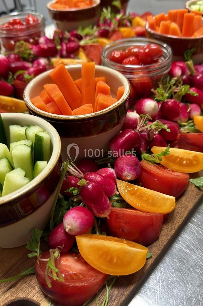 Plateau de légumes frais comprenant radis, tomates, carottes et concombres, disposés autour de bols en céramique.