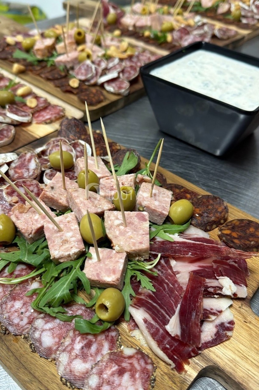 Plateau de charcuterie variée avec olives, roquette et terrine, accompagné d'une sauce blanche en arrière-plan.