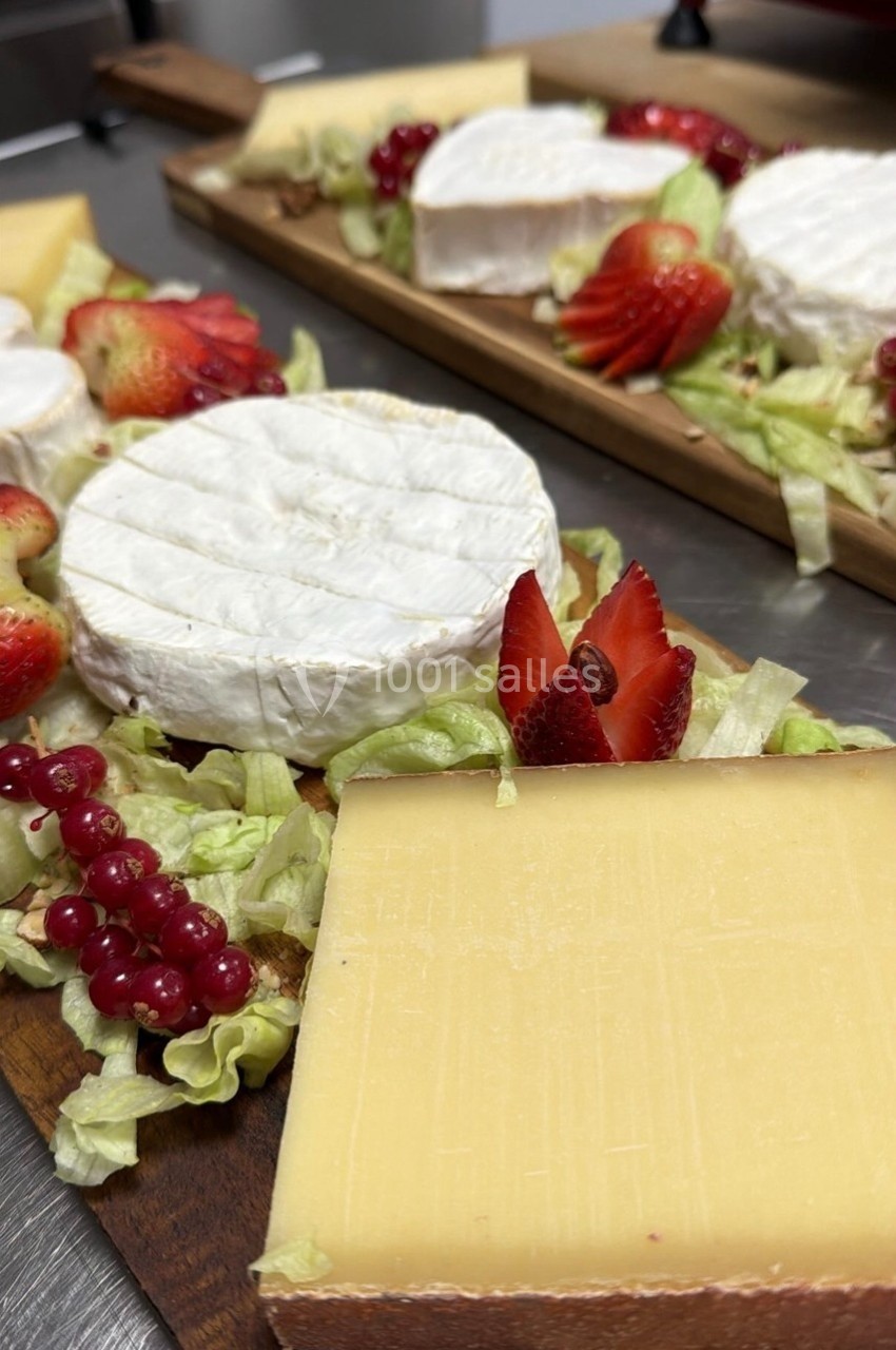Plateaux de fromages variés avec brie, comté, fraises, groseilles et salade sur une table en bois.