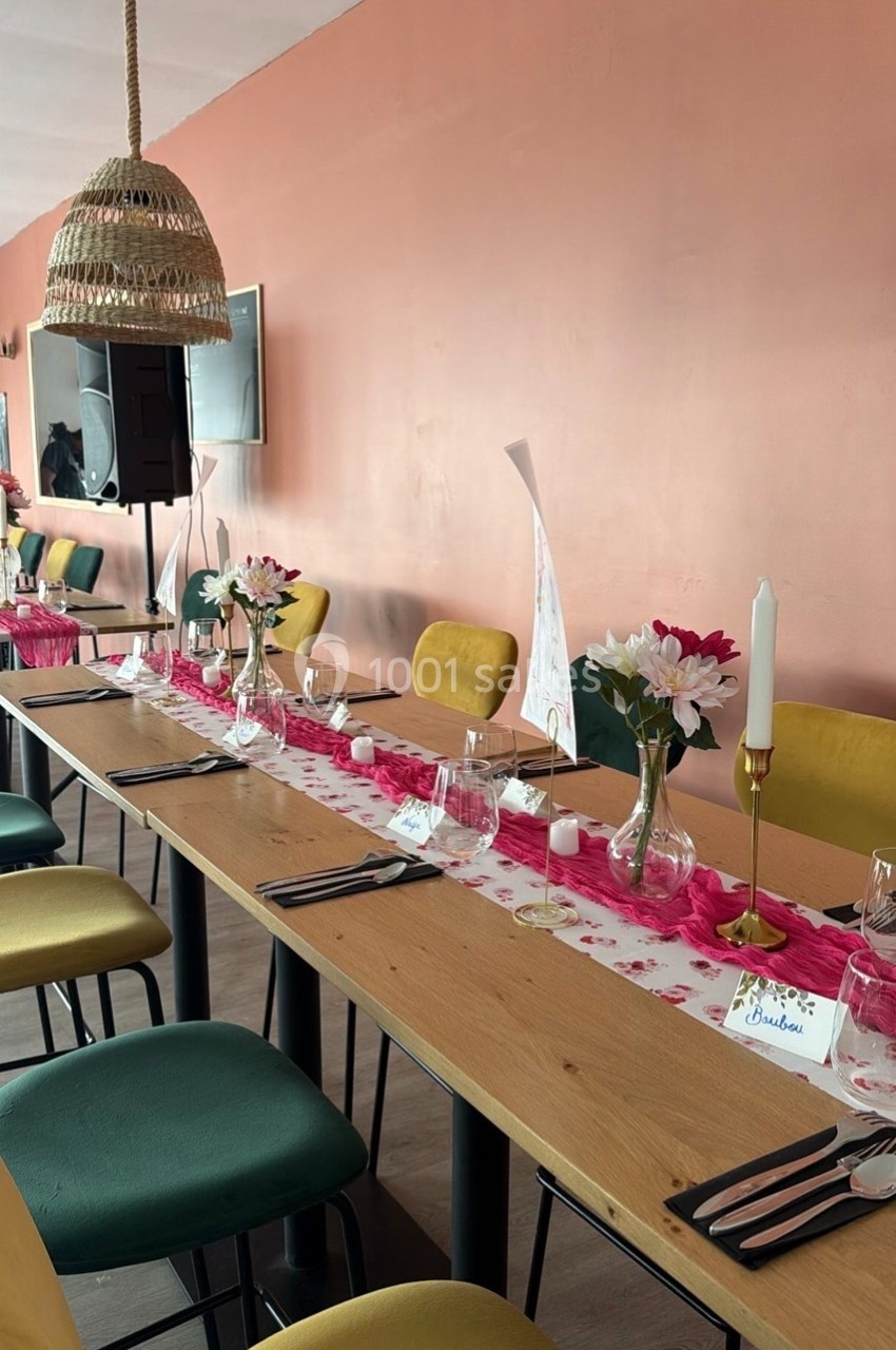 Table décorée pour un repas, avec chemins de table roses, fleurs, bougies et chaises jaunes et vertes.