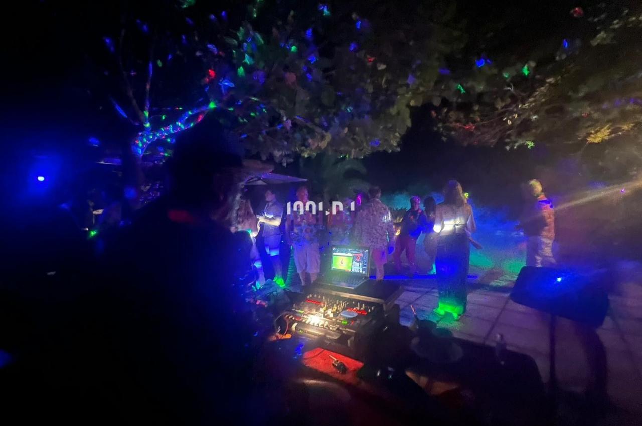 Personnes dansant de nuit sous des lumières colorées, avec une table de mixage visible au premier plan.