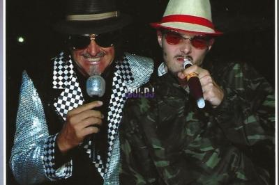 Miniature DJ Hyères (Var) - Prom'Art DJ Didou #15 Des artistes en costumes brillants dansent sur une scène illuminée par des projecteurs colorés et un écran lumineux.