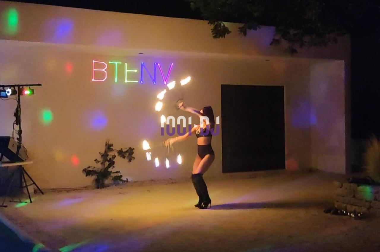 Personne jonglant avec des objets lumineux dans une cour éclairée par des lumières colorées, de nuit.