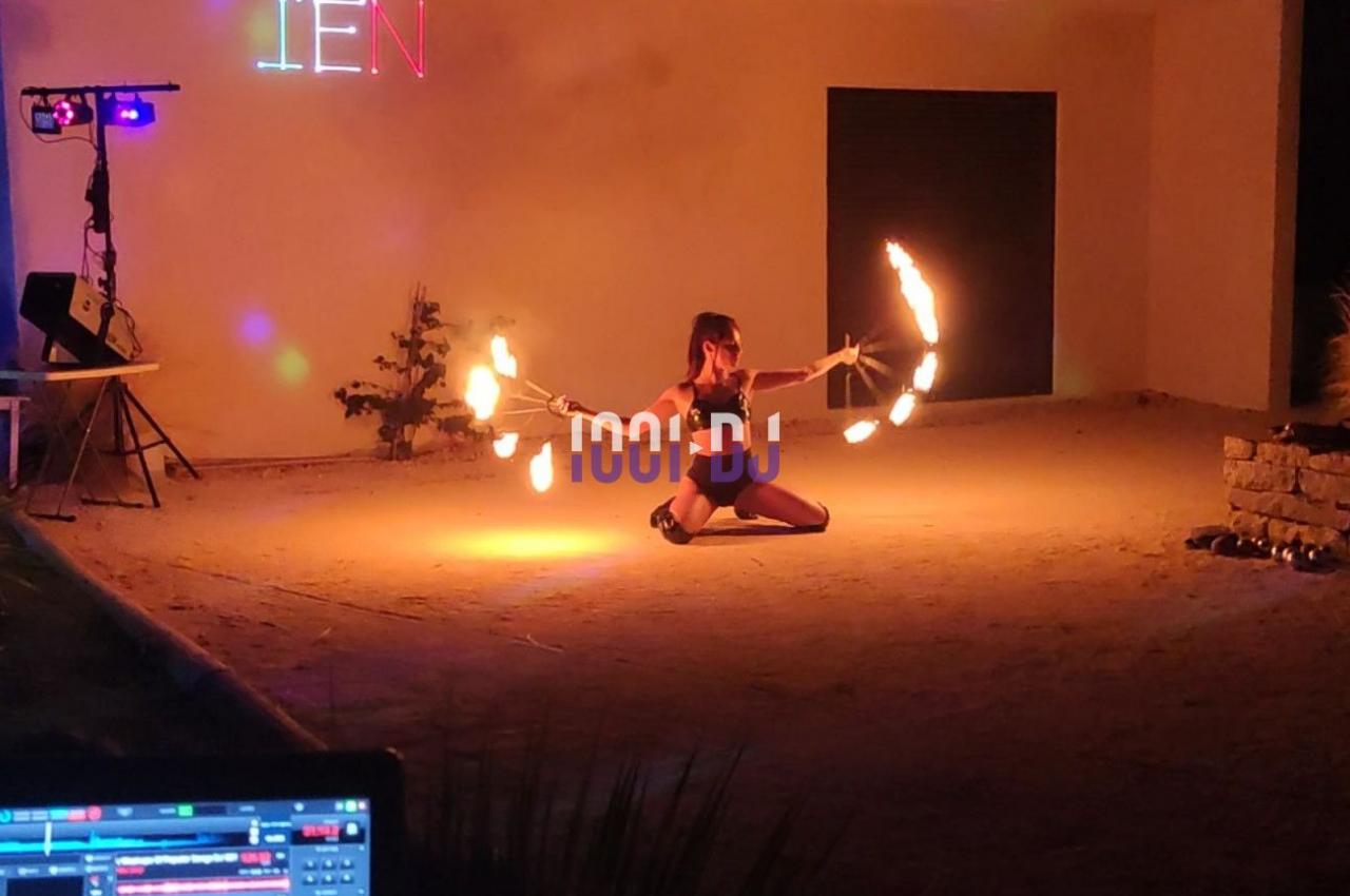 Personne jonglant avec des bâtons de feu dans une ambiance nocturne, éclairée par des lumières colorées.