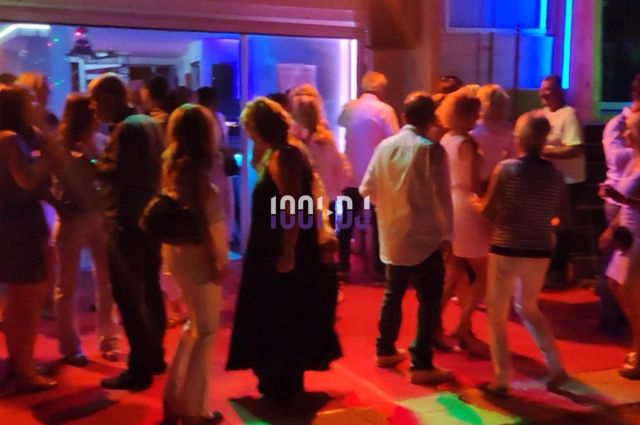 Groupe de personnes dansant et discutant dans un espace éclairé par des lumières colorées en soirée.