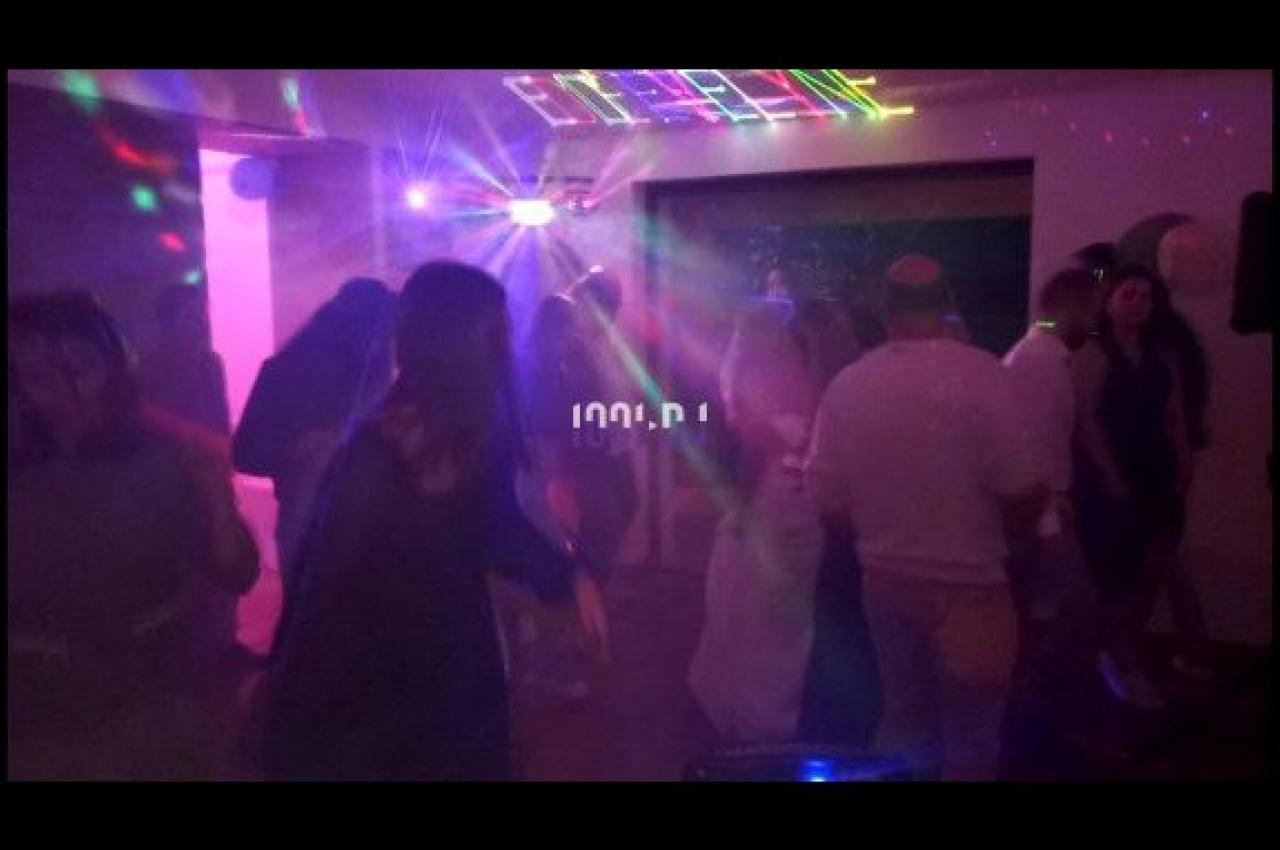 Des personnes dansent dans une salle sombre éclairée par des lumières colorées et un éclairage de fête.