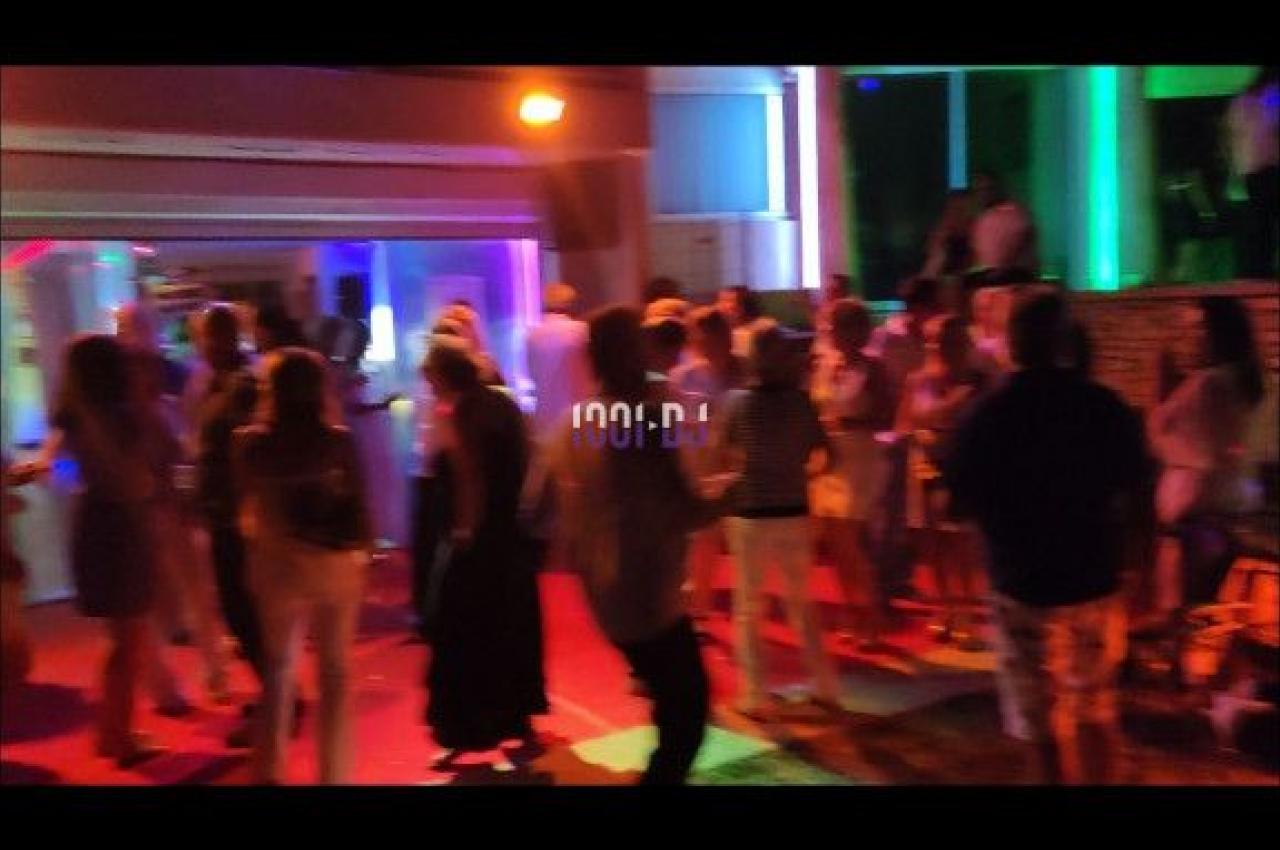 Groupe de personnes dansant et discutant dans un espace extérieur éclairé par des lumières colorées.