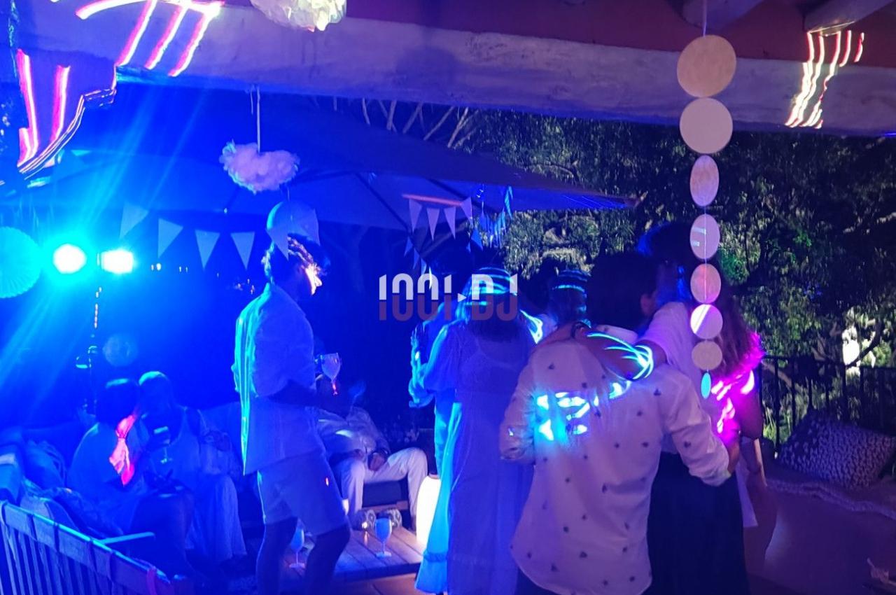 Personnes dansant et discutant lors d'une fête en soirée, éclairée par des lumières colorées et une décoration festive.