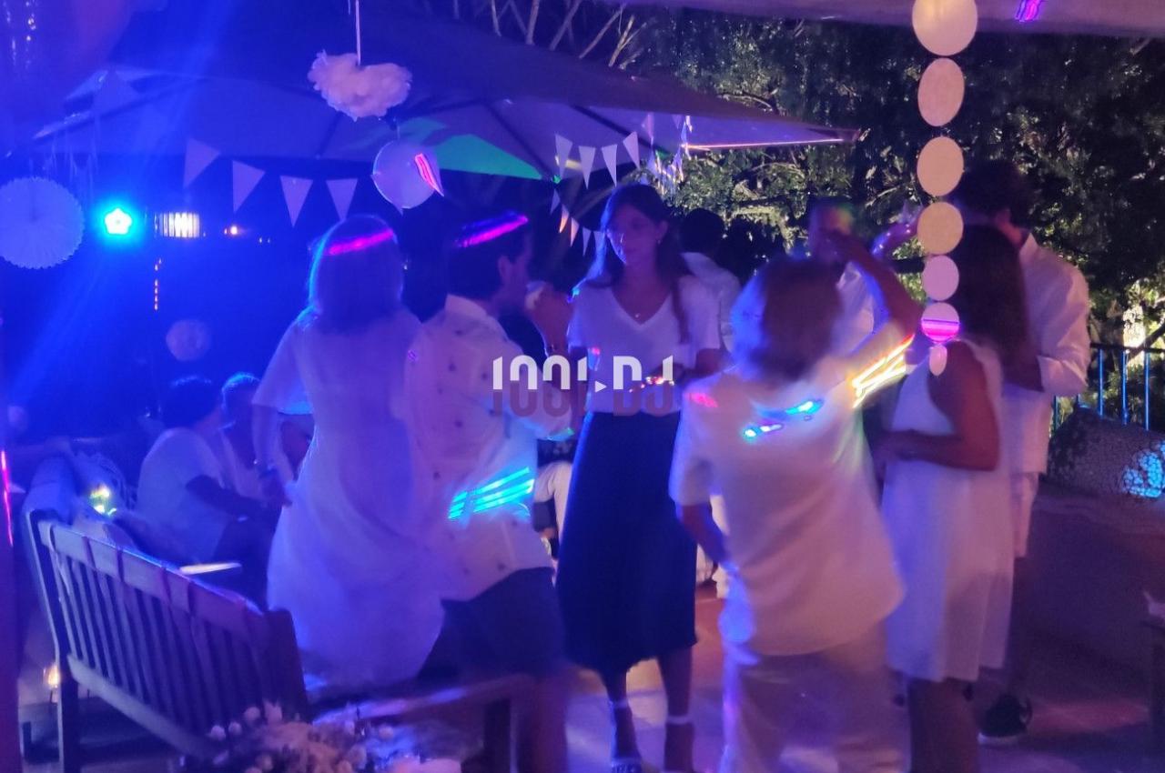 Des personnes dansent sous des lumières colorées lors d'une fête en extérieur, entourées de décorations festives.