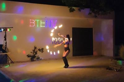 Des artistes en costumes brillants dansent sur une scène illuminée par des projecteurs colorés et un écran lumineux.