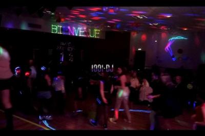 Des artistes en costumes brillants dansent sur une scène illuminée par des projecteurs colorés et un écran lumineux.