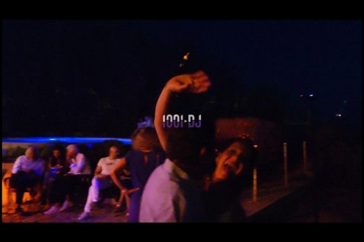 Personnes dansant en extérieur la nuit, avec des lumières tamisées et d'autres assises en arrière-plan.